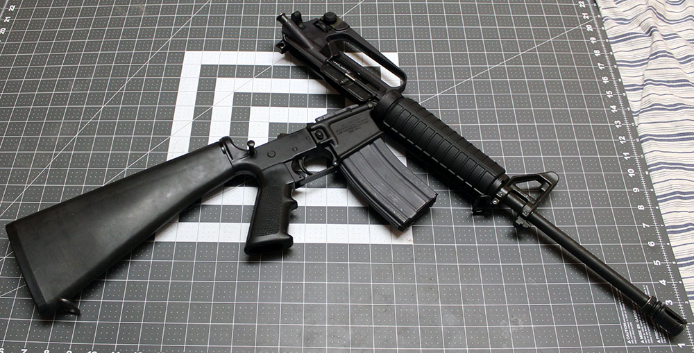 AR-15 with the rear pin pulled and the top hinged open, lying on its left side